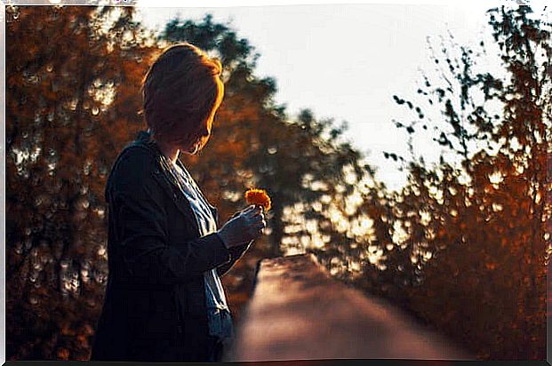 A woman looks down while holding a flower.